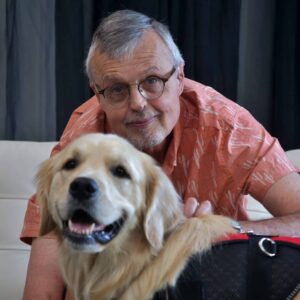 Caucasian man with glasses and orange shirt hugging fluffy golden retriever