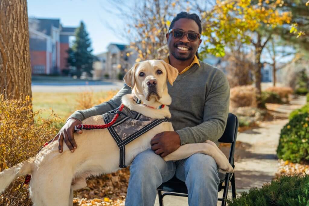 U.S. Army veteran man with a yellow Labrador Retriever wearing an army camo printed service dog harness. 