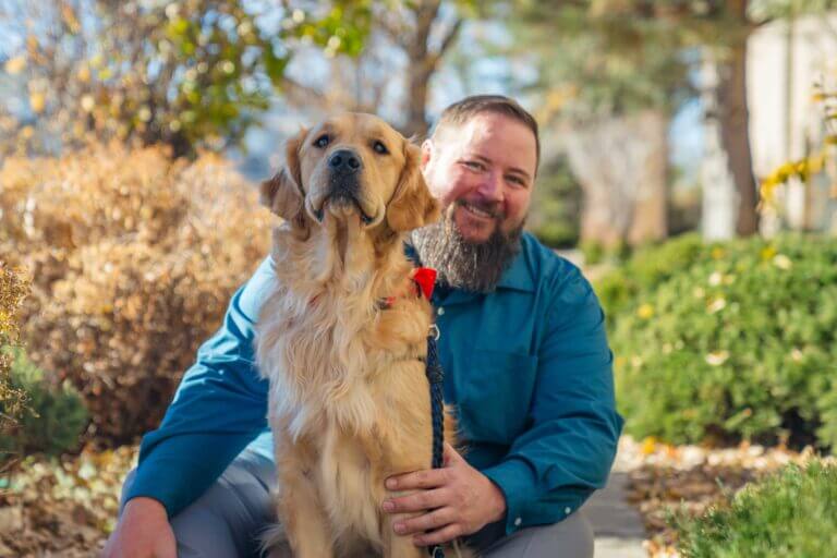 A man in a blue shirt sitting with a golden retriever dog sitting on his lap.