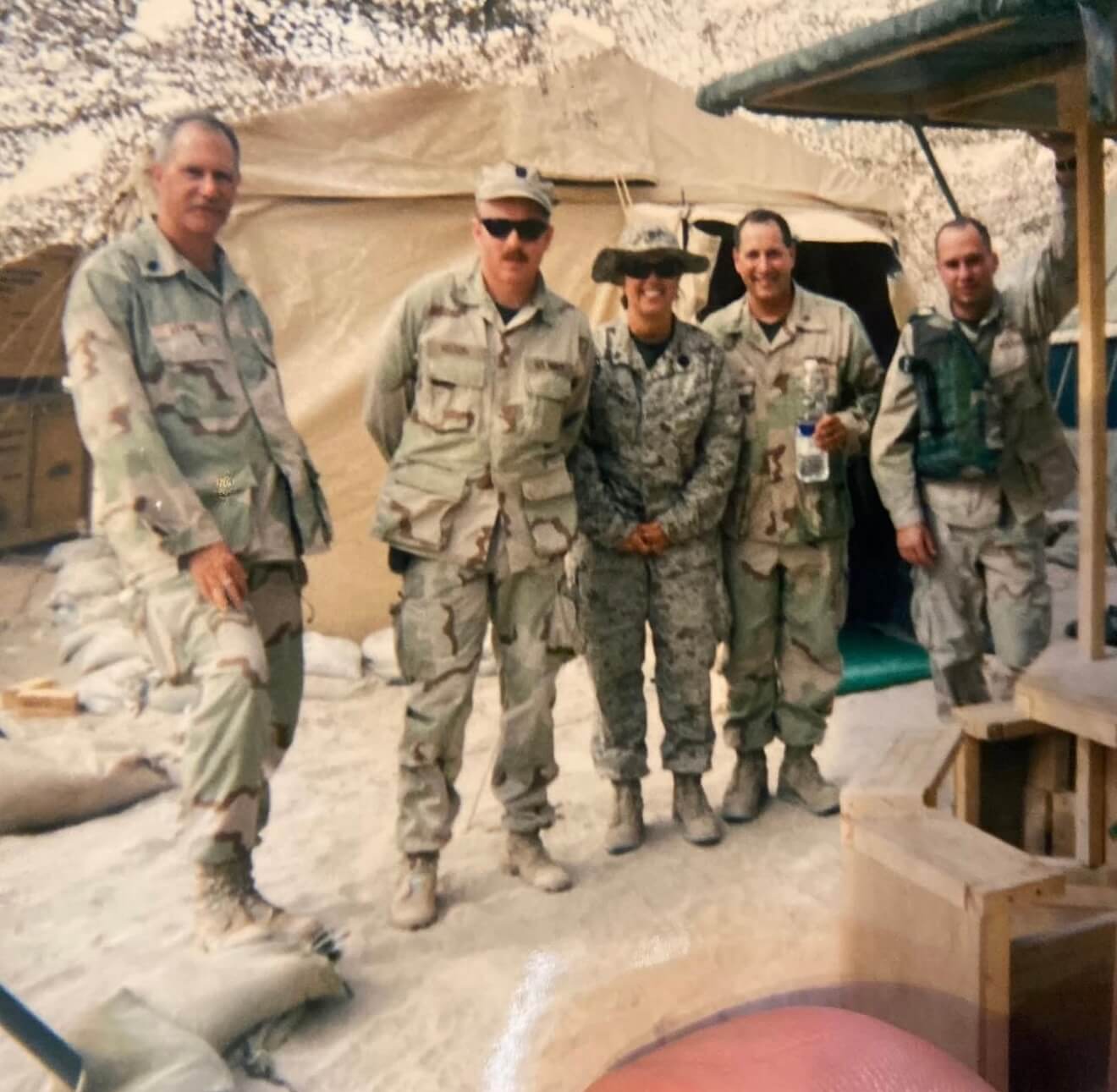 Five soldiers in uniform standing in front of tent on deployment. 