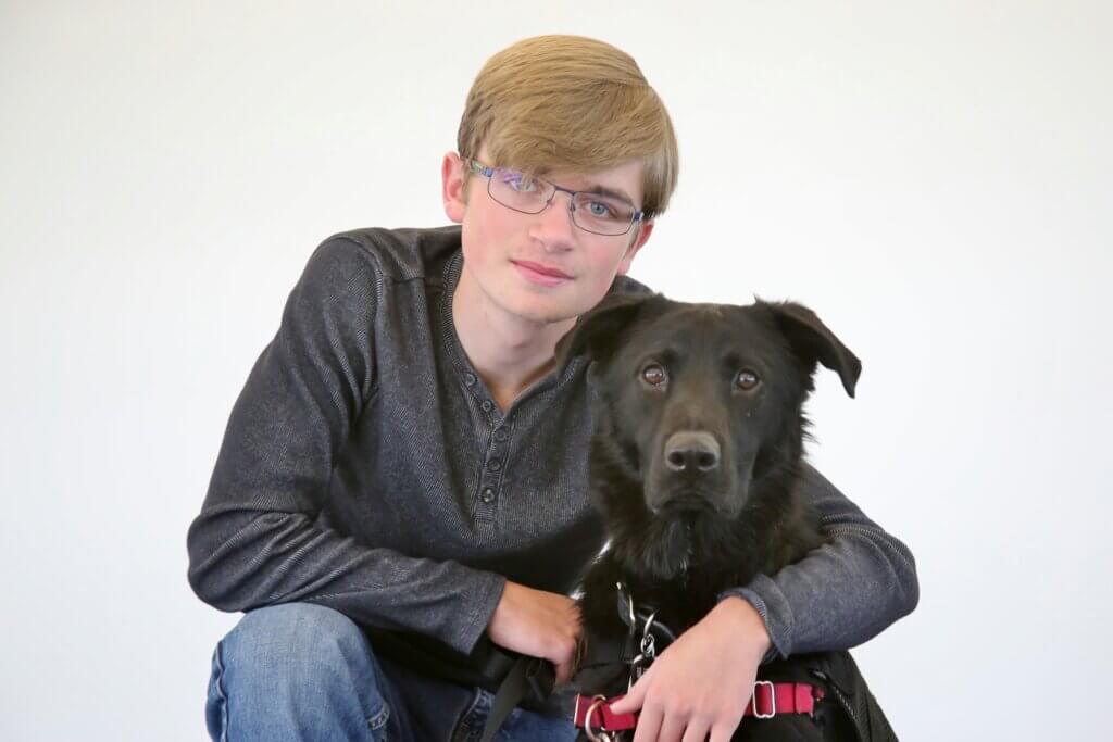 A young man wearing glasses with his black shepherd mix Freedom Service Dog.