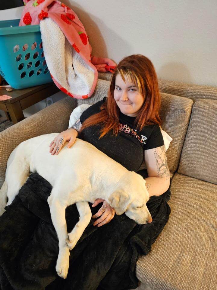 Kiya sitting on a couch with her yellow Labrador Retriever sitting on her lap. 
