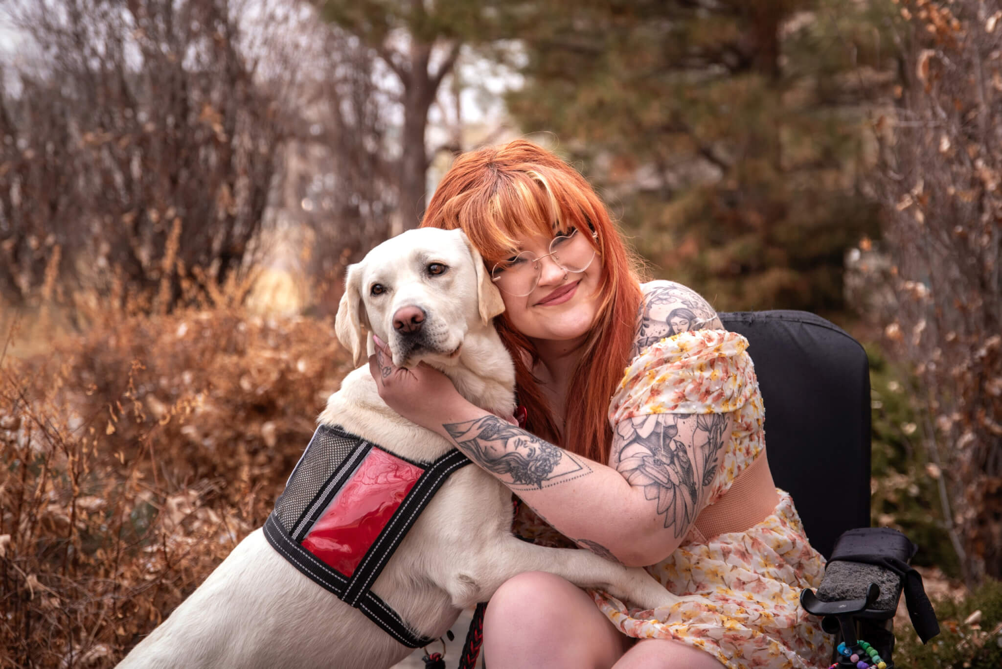 A young woman with disabilities in a wheelchair hugging her yellow Labrador retriever service dog wearing a red Freedom Service Dogs service dog vest.