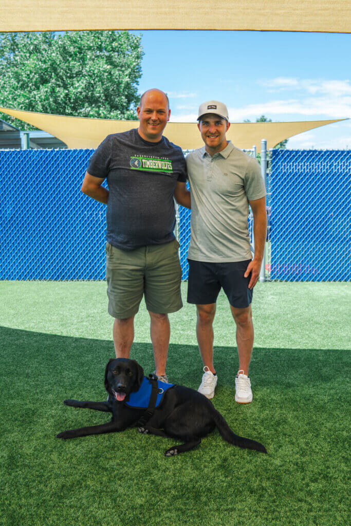 SRO Kevin standing with Colorado Avalanche Defenseman Devon Toews and FSD Facility Dog Jack, a black Labrador retriever wearing a blue working dog vest.