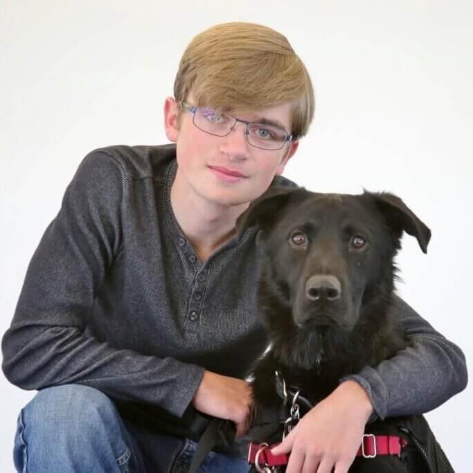 A young man wearing glasses with his black shepherd mix Freedom Service Dog.