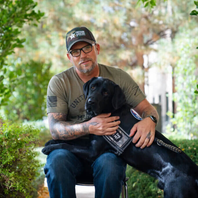 Man with black Labrador Retriever wearing a Freedom Service Dogs service dog vest performing deep pressure therapy